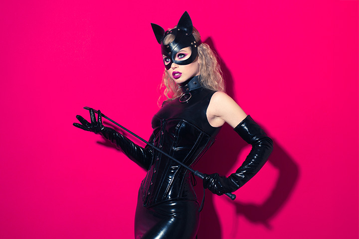 Domina in Fetischkleidung mit Peitsche und Maske